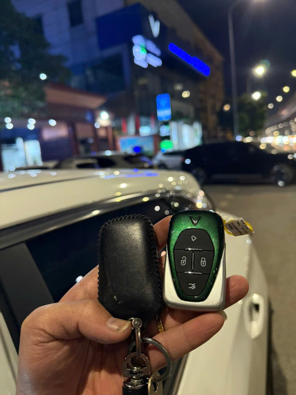 Chìa khóa ô tô VinFast màu xanh đen trên tay người dùng trước chiếc xe màu trắng ban đêm