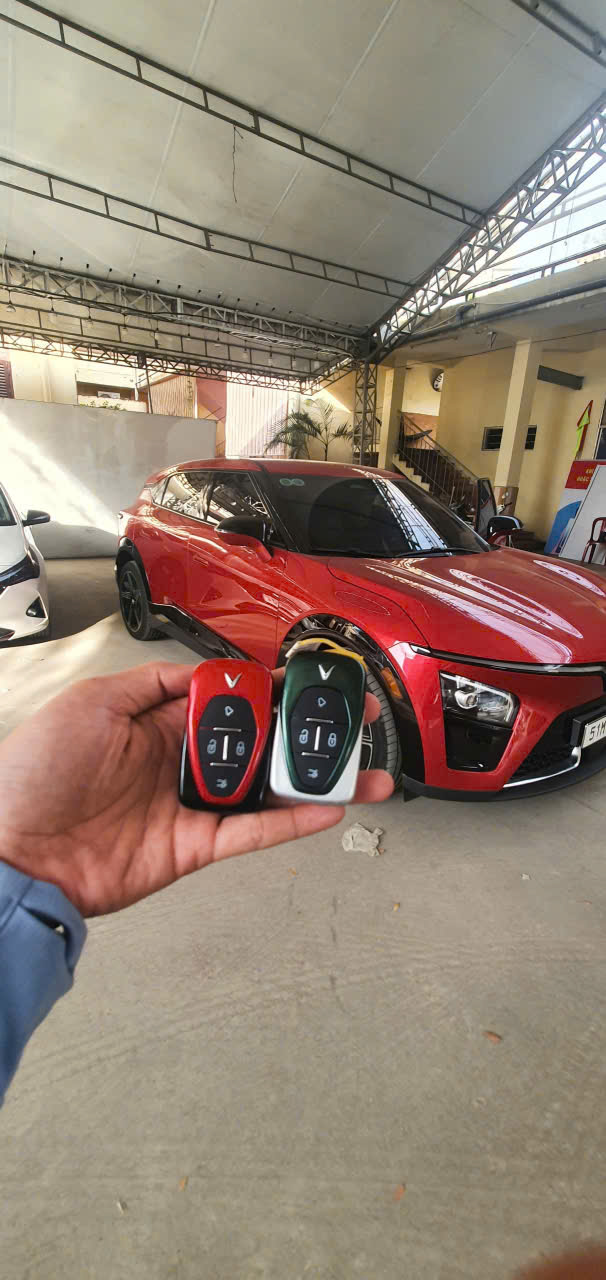 Hai chìa khóa ô tô VinFast trên tay phía trước xe VinFast màu đỏ trong gara