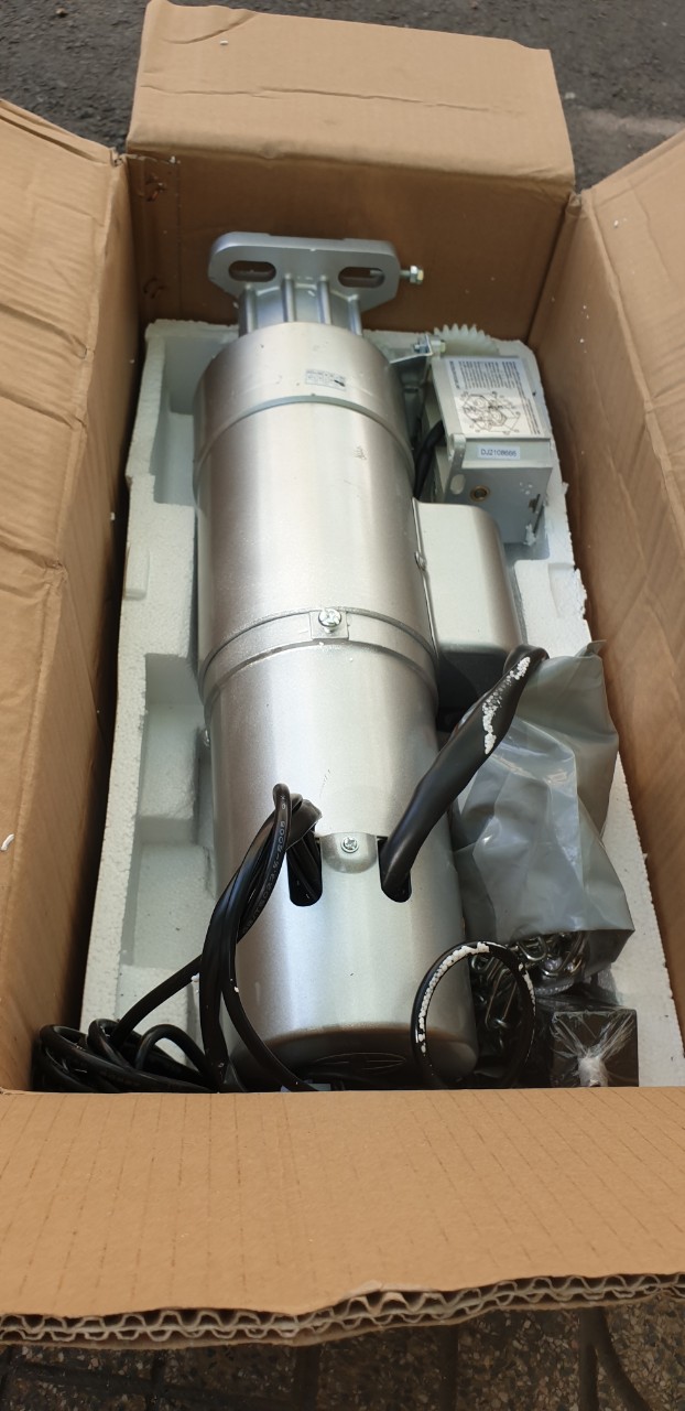 Mô tơ cửa cuốn màu bạc kèm phụ kiện và dây điện được đóng gói trong thùng carton