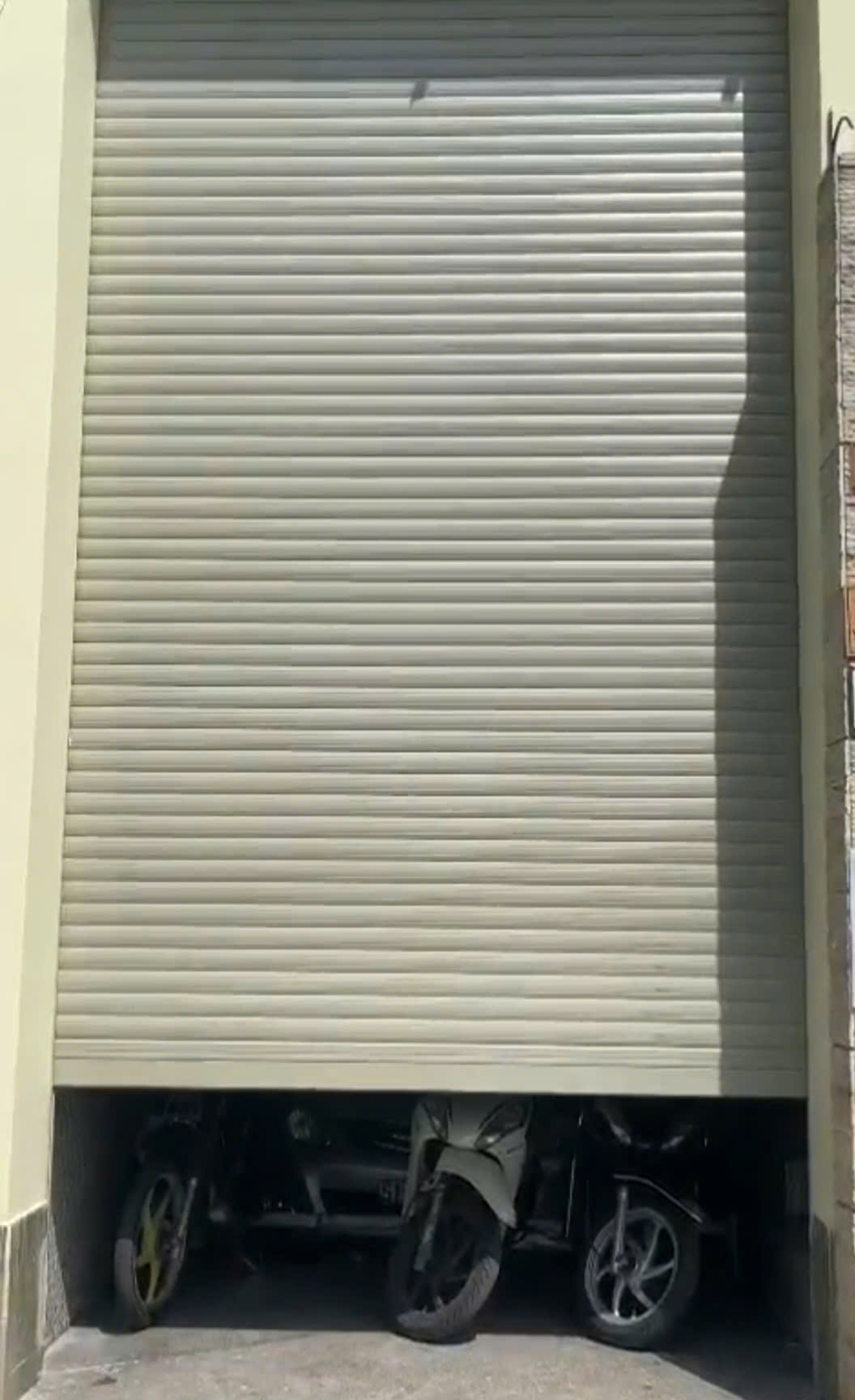 Cửa cuốn nhà xe đang hạ xuống, phía dưới là các xe máy và ô tô đậu bên trong