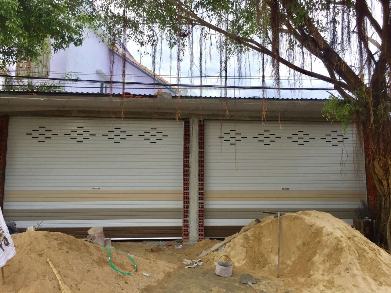 Cửa cuốn tôn màu trắng kem hoa văn ô thoáng lắp đặt cho mặt tiền nhà đang xây dựng