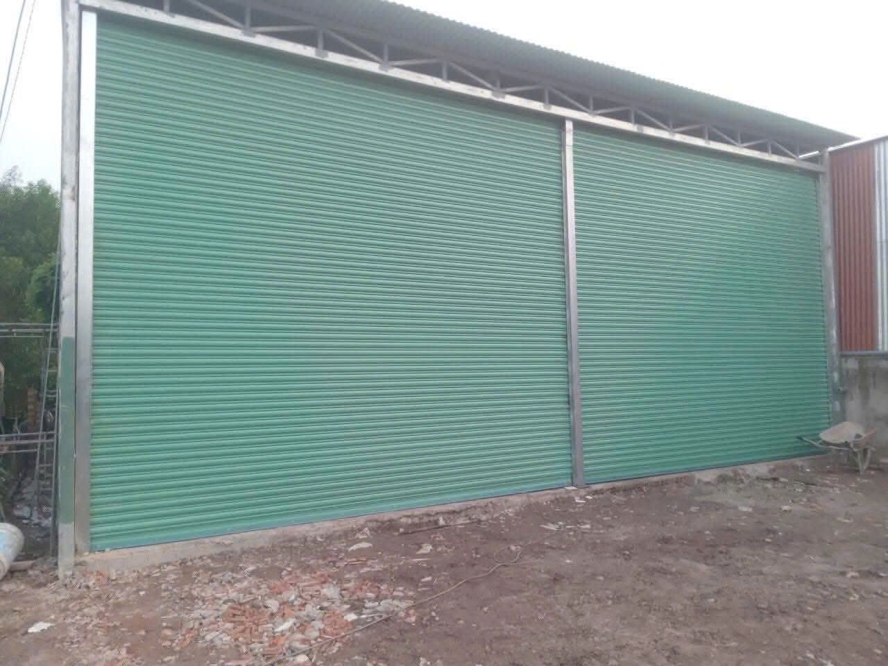 Cửa cuốn tôn màu xanh cho nhà xưởng khung thép, mặt tiền rộng đang trong quá trình hoàn thiện