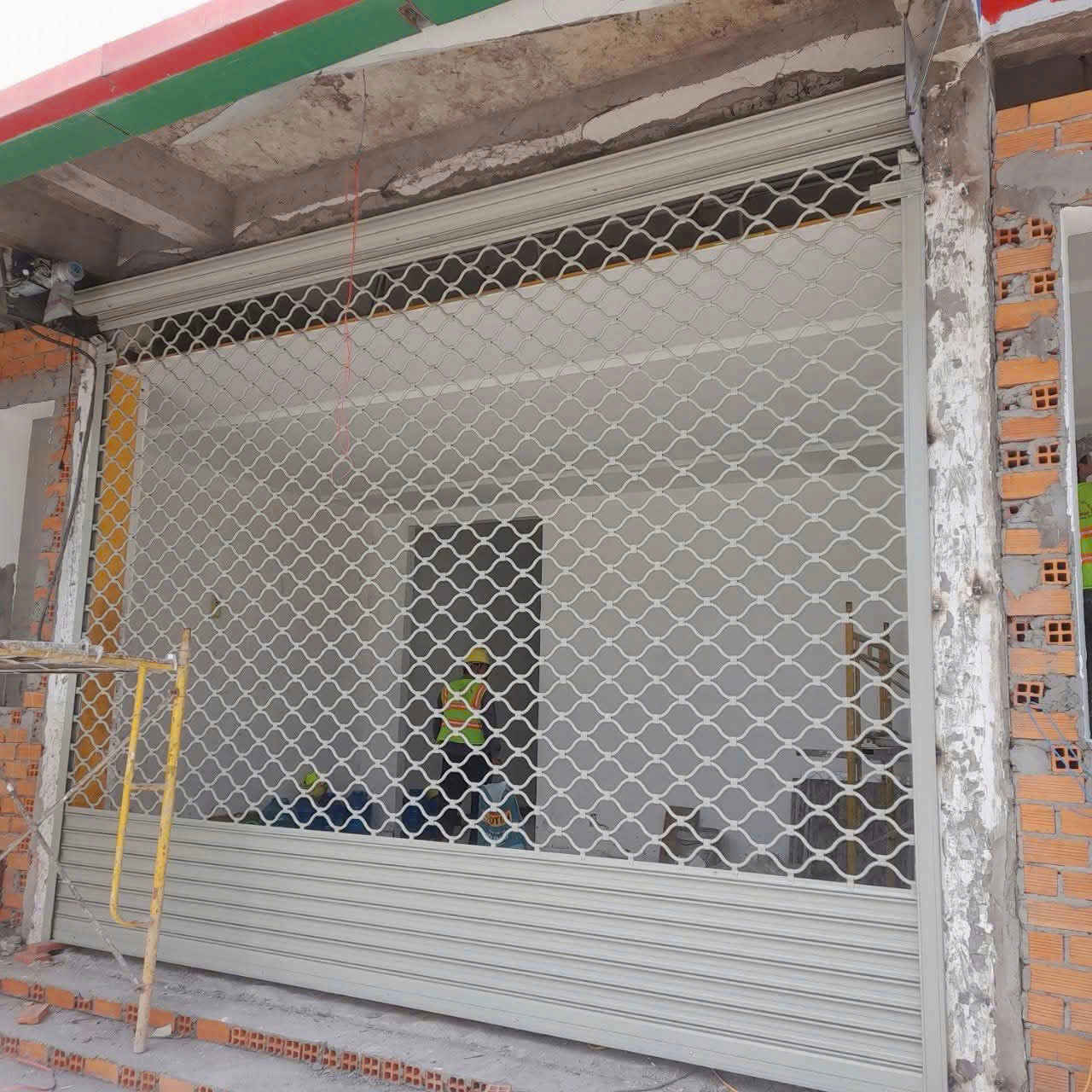 Cửa cuốn lưới mắt võng màu xám đang lắp đặt cho mặt tiền cửa hàng đang xây dựng
