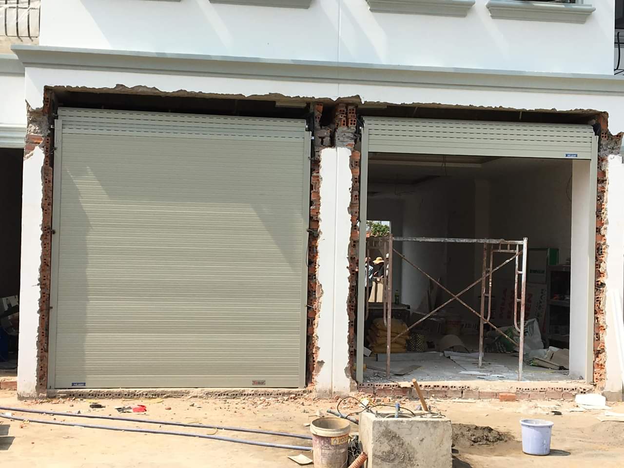 Cửa cuốn tấm liền màu kem đang lắp đặt cho mặt tiền nhà phố đang thi công