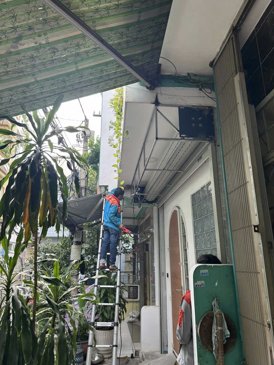 Kỹ thuật viên đứng trên thang nhôm lắp đặt sửa chữa hệ thống camera an ninh trước cửa nhà