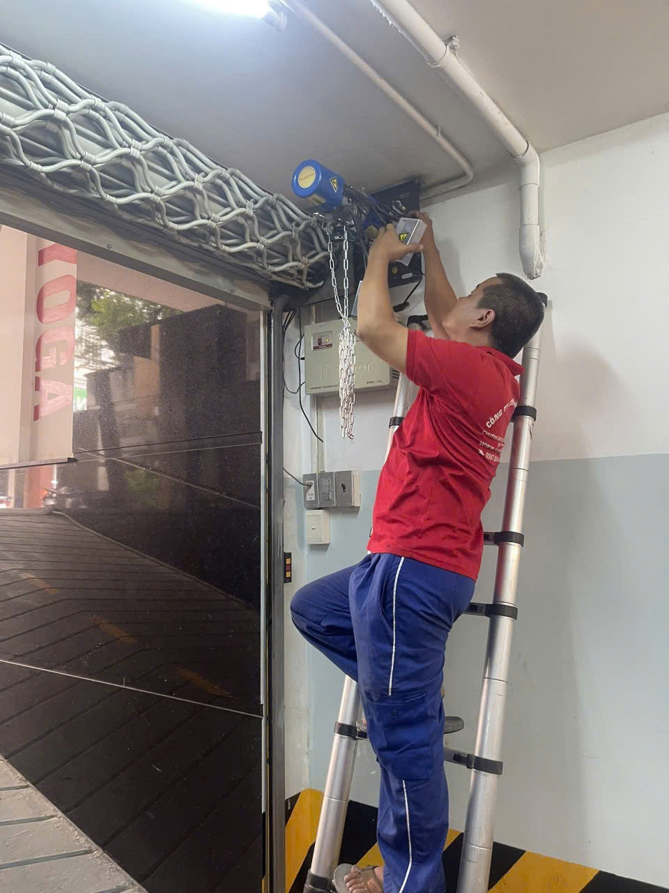 Kỹ thuật viên đứng trên thang sửa chữa motor cửa cuốn tự động trong gara nhà xe