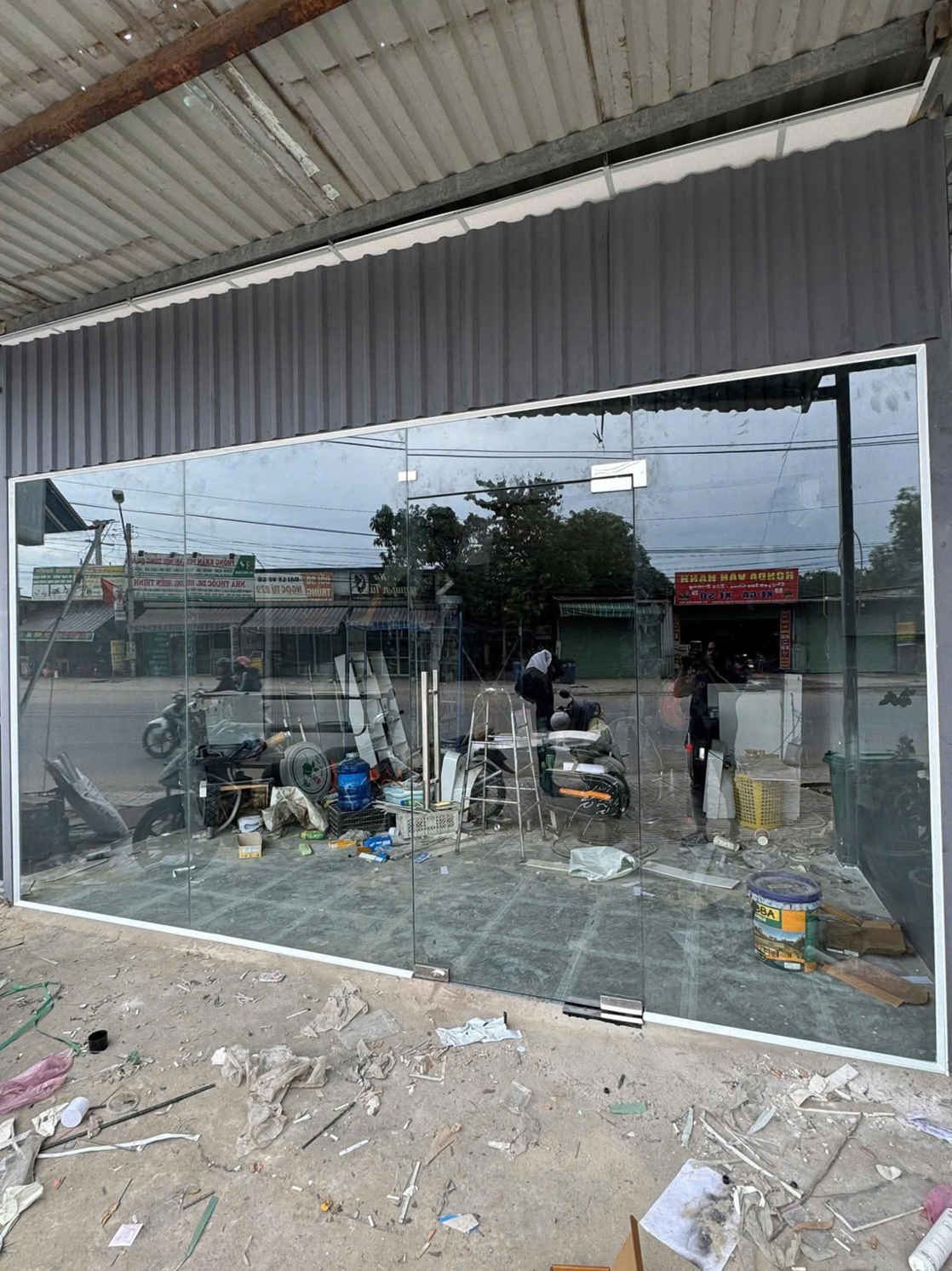 Cửa kính cường lực mặt tiền cửa hàng đang thi công, khung nhôm và sàn còn ngổn ngang vật liệu