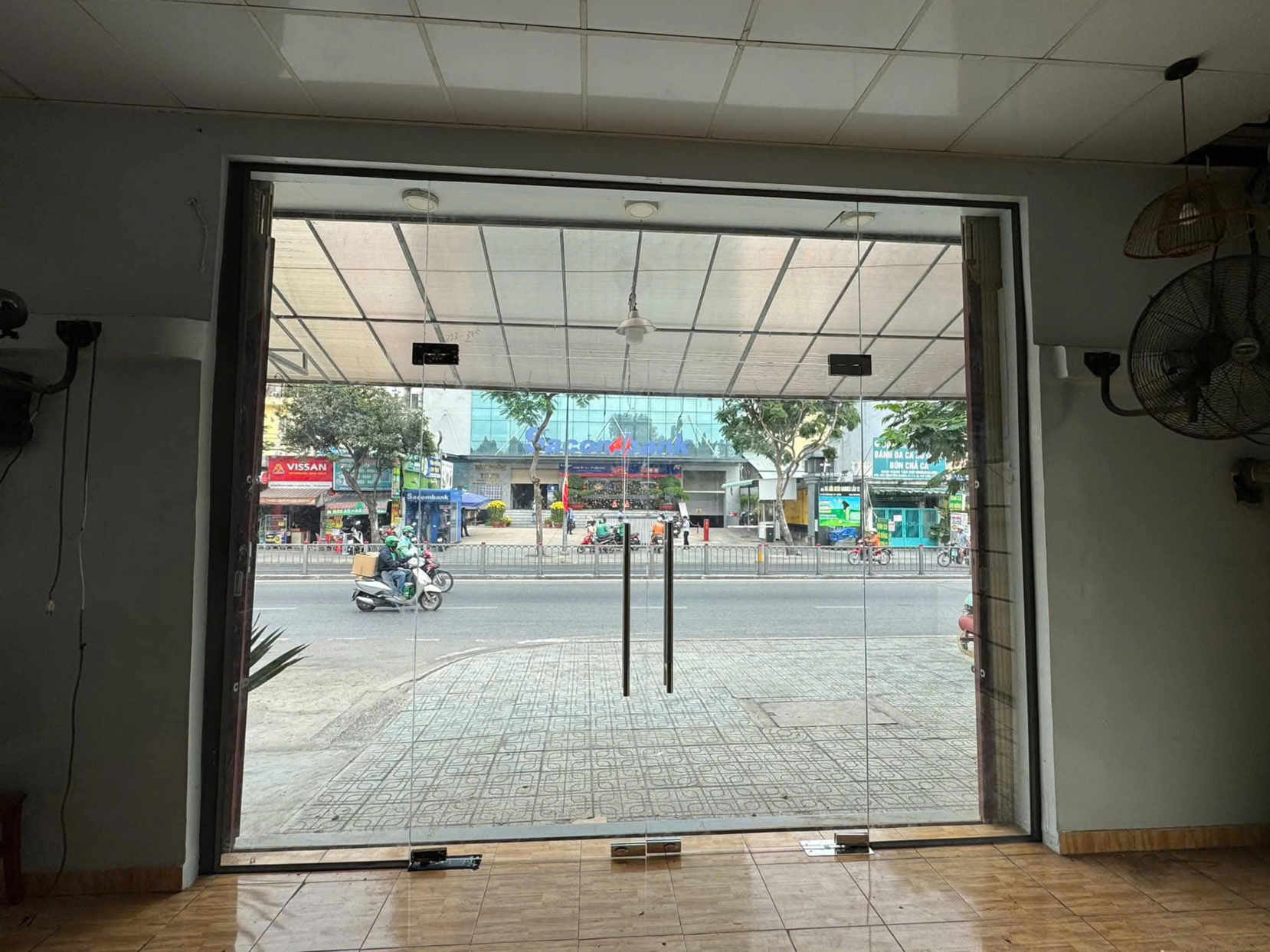 Cửa kính cường lực hai cánh khung nhôm nhìn ra đường phố đông xe cộ