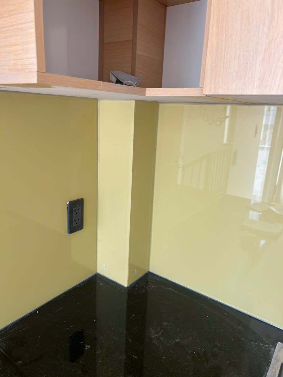 Kính ốp bếp màu vàng kem với mặt bàn đá đen và ổ cắm điện âm tường trong bếp hiện đại