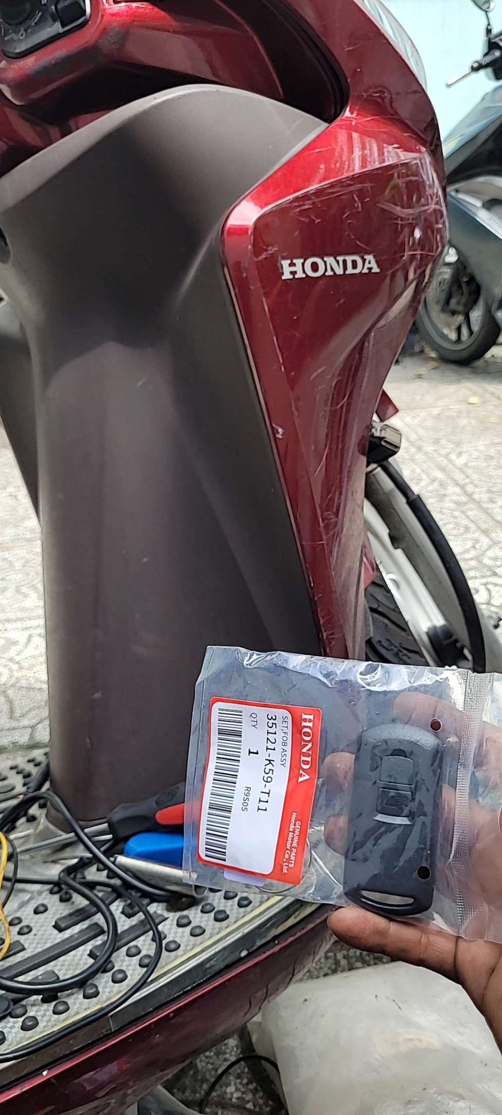 Chìa khóa remote Honda chính hãng mã 35121-K59-T11 trên tay cạnh xe máy Honda màu đỏ