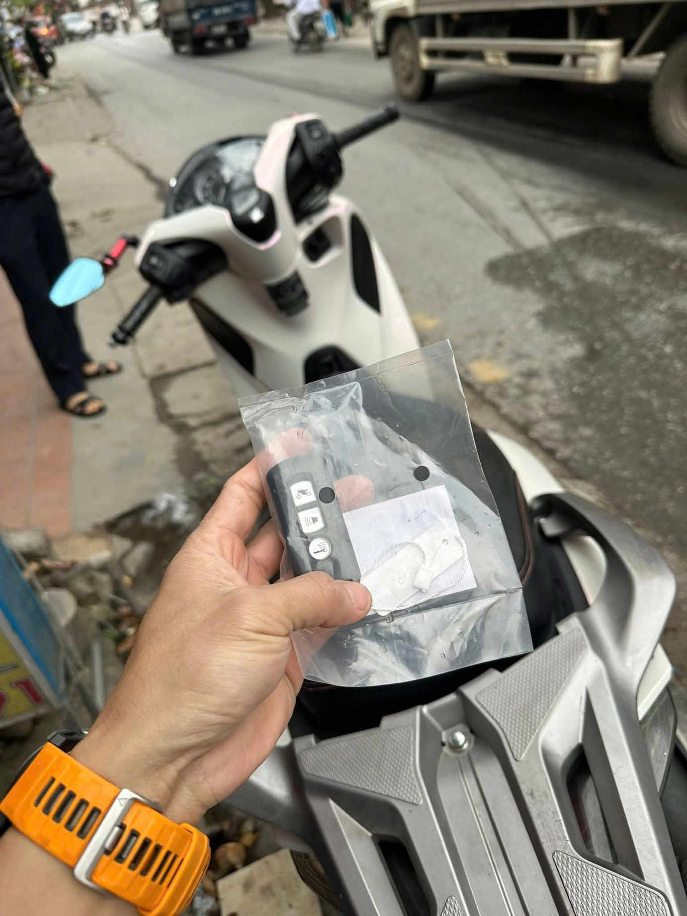 Tay cầm điều khiển khóa thông minh xe máy trong túi nilon trước yên xe tay ga trắng trên vỉa hè