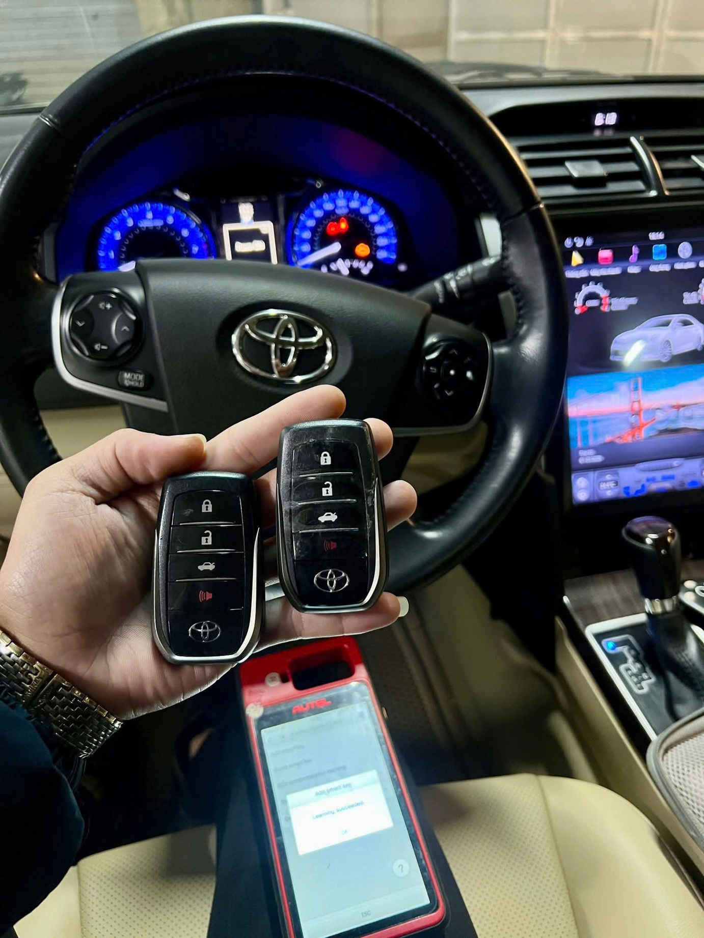 Hai chìa khóa thông minh ô tô Toyota trên tay trong khoang lái với vô lăng và màn hình trung tâm