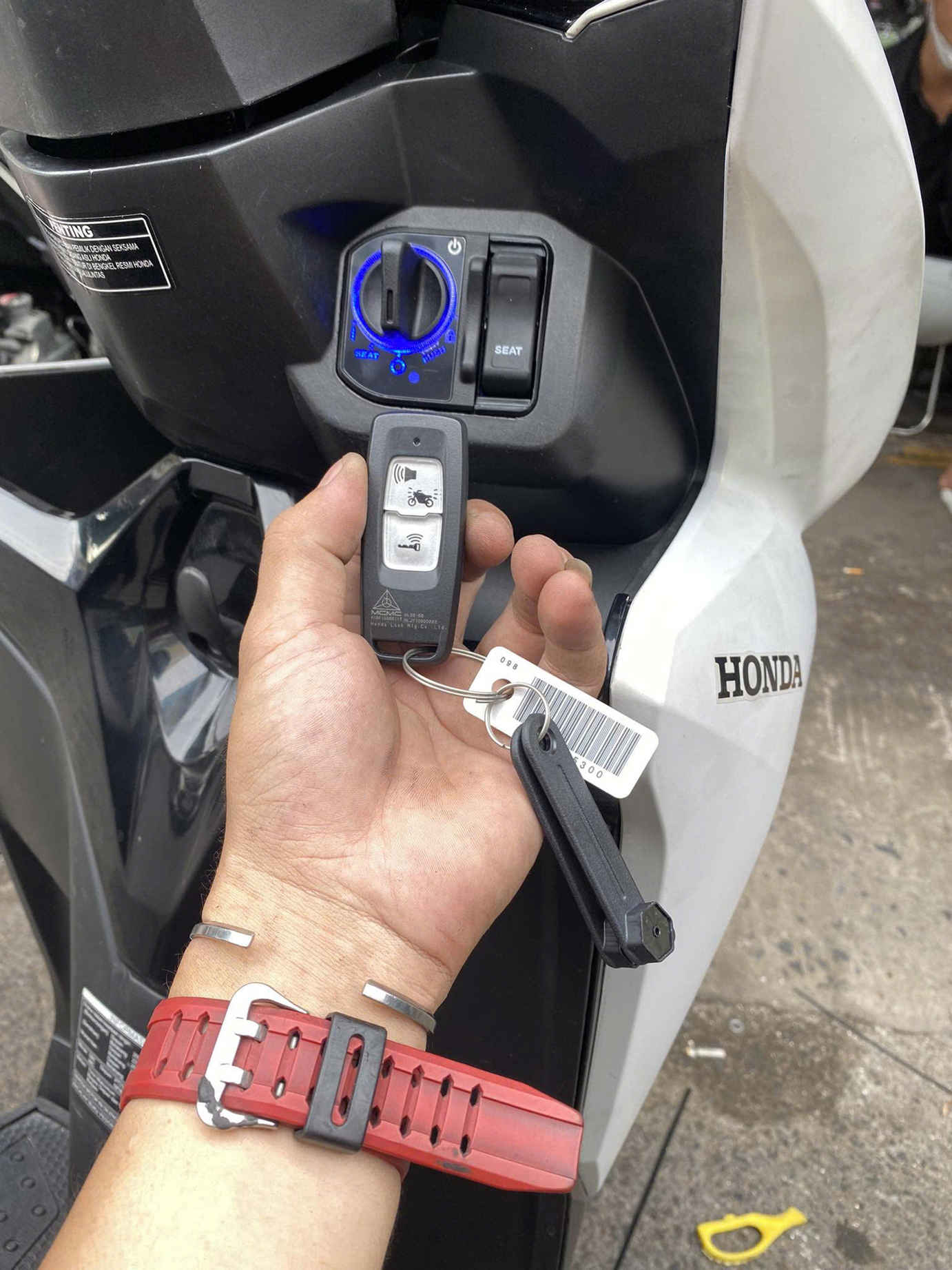 Chìa khóa smartkey xe máy Honda đang được cầm trước ổ khóa thông minh trên thân xe
