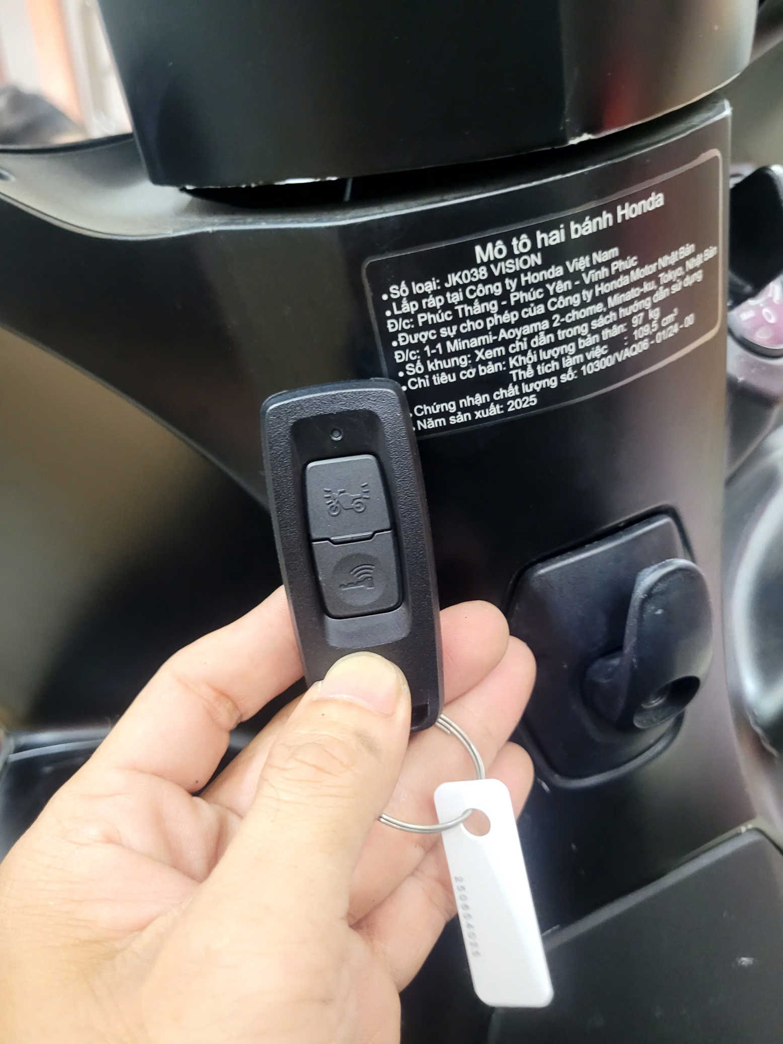 Chìa khóa thông minh xe máy Honda Vision trên tay người dùng gần tem thông số kỹ thuật
