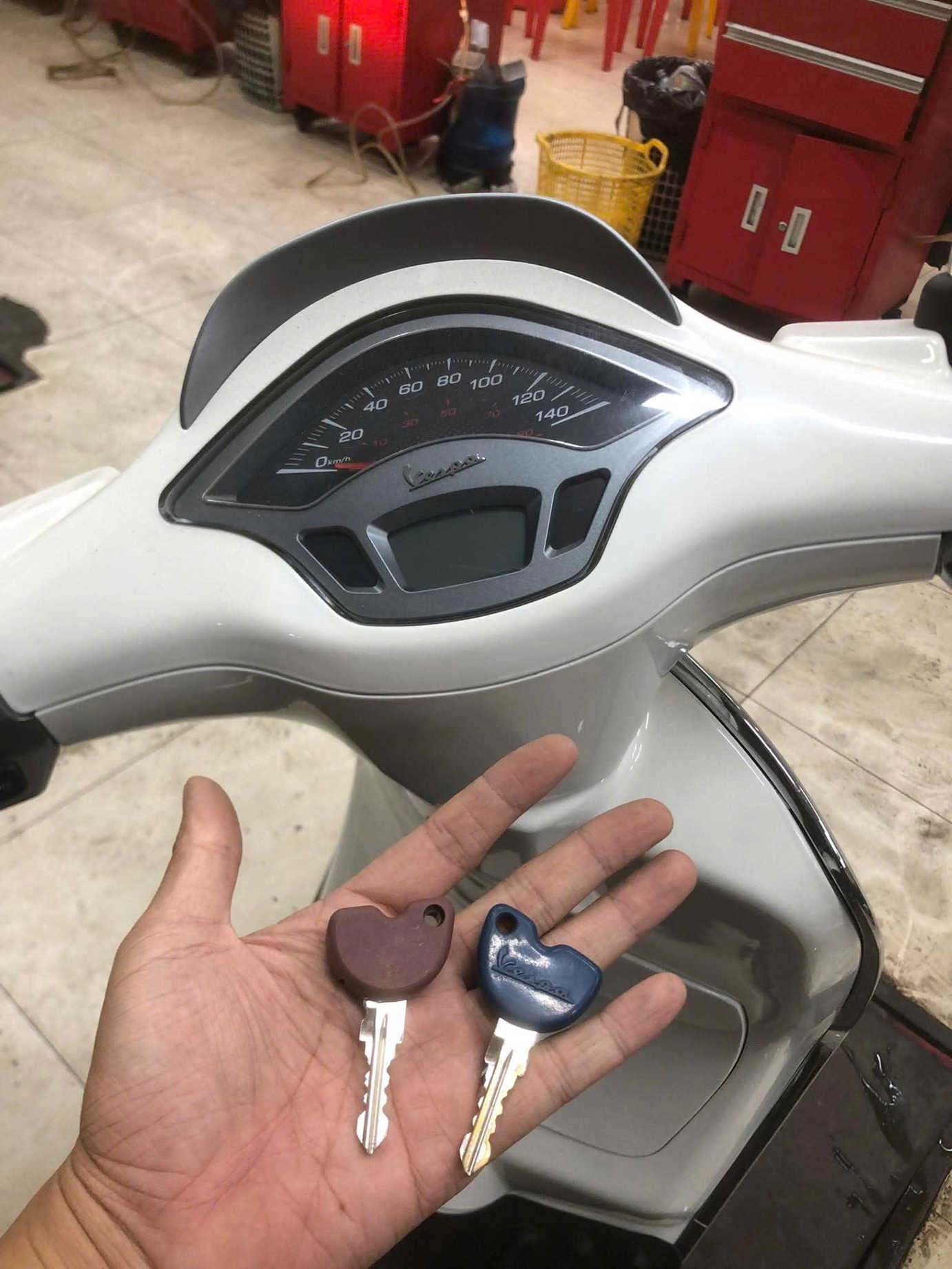 Chìa khóa Vespa trên tay trước bảng đồng hồ xe trong xưởng sửa chữa