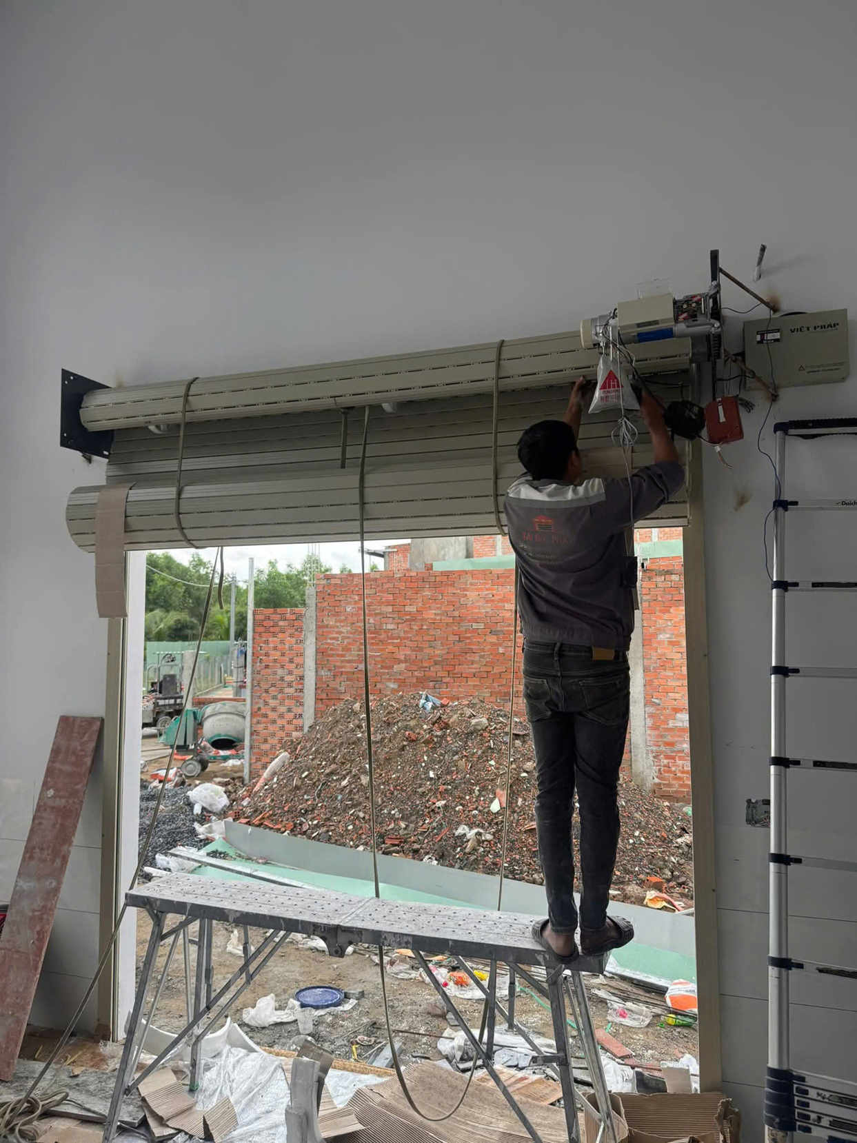 Thợ kỹ thuật đang lắp đặt cửa cuốn tự động cho mặt tiền nhà đang xây dựng