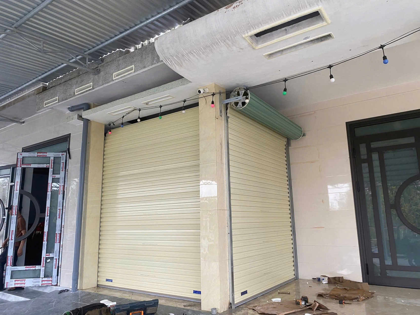 Cửa cuốn tôn màu kem lắp đặt tại mặt tiền nhà, kèm hệ thống mô tơ và ray dẫn hướng