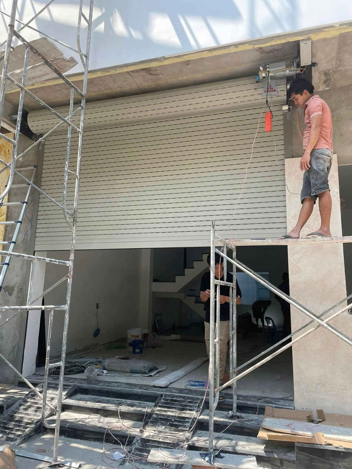 Thợ đang lắp đặt sửa cửa cuốn tự động màu trắng cho mặt tiền nhà phố đang xây dựng