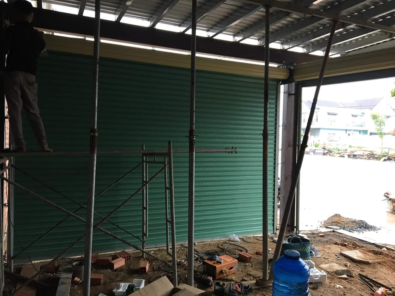 Cửa cuốn tôn màu xanh đang được lắp đặt tại công trình xây dựng