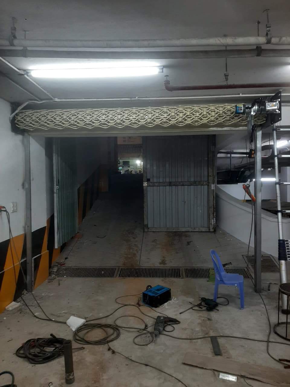 Cửa cuốn gara đang thi công với motor kéo và dụng cụ sửa chữa bày trên nền bê tông
