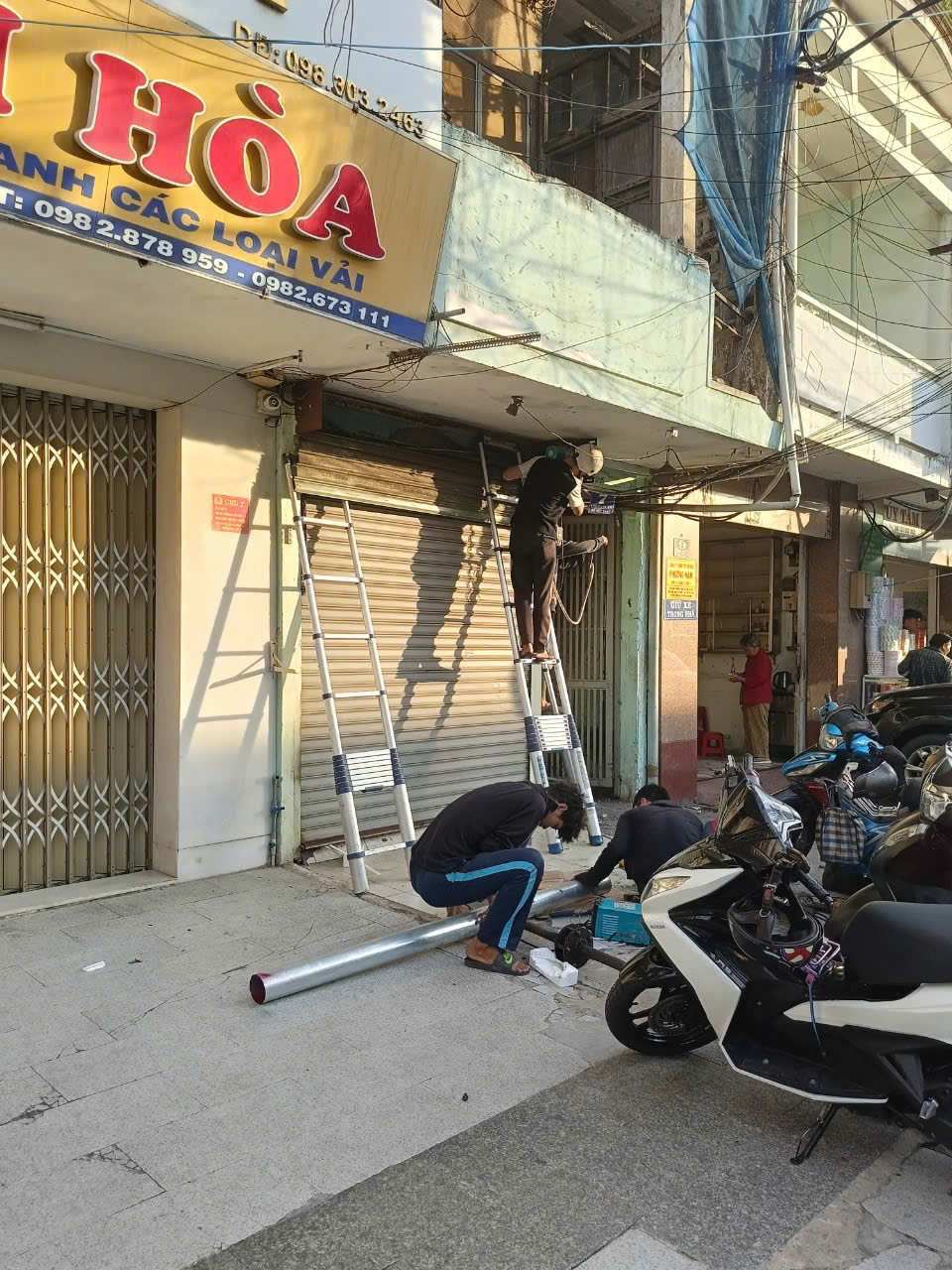 Thợ đang lắp đặt ống dẫn và sửa chữa cửa cuốn trước cửa hàng mặt phố