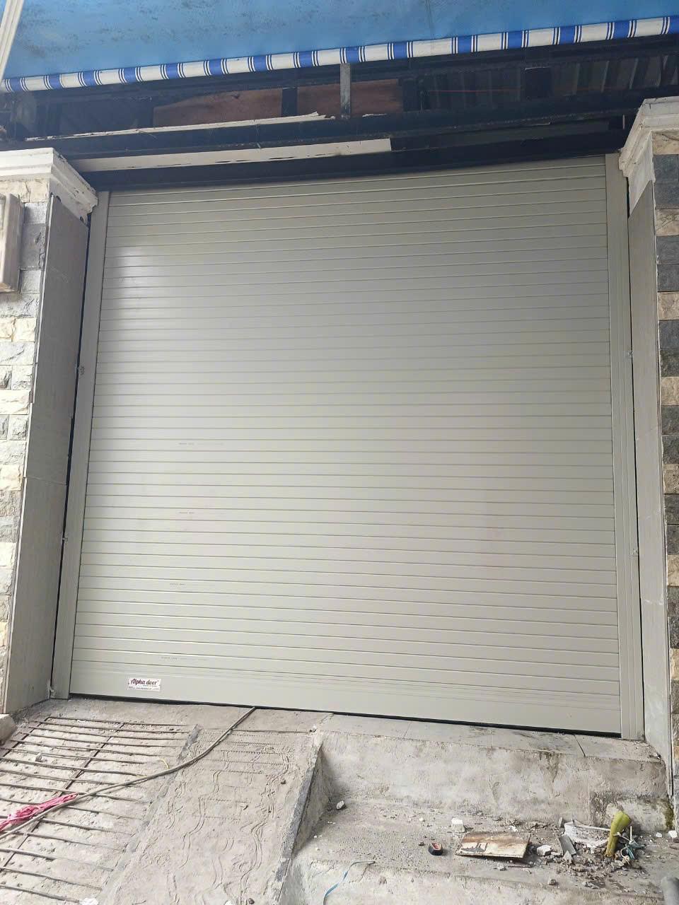 Cửa cuốn tôn màu xám lắp đặt cho mặt tiền nhà đang trong quá trình hoàn thiện nền bê tông