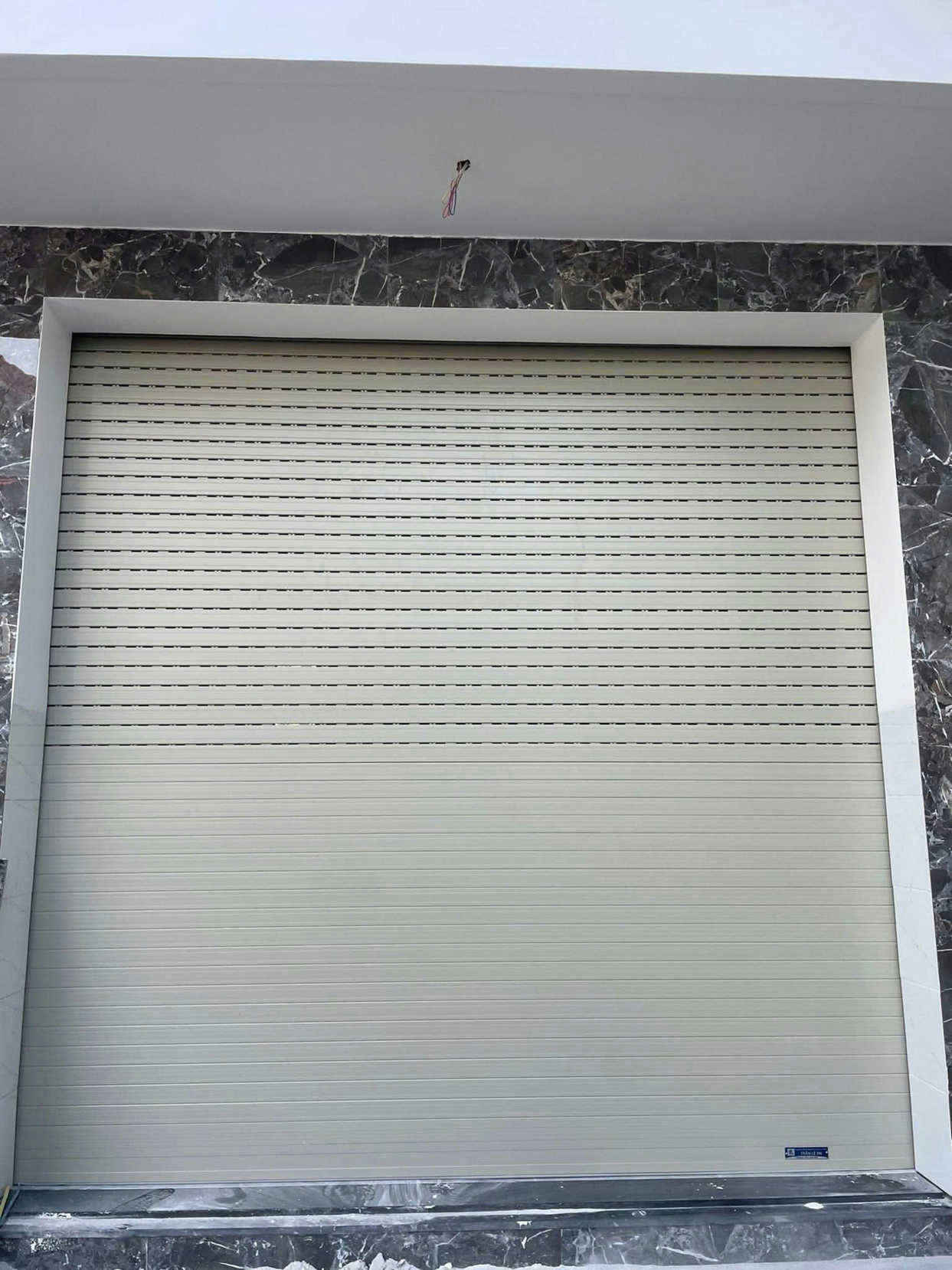 Cửa cuốn khe thoáng màu kem lắp đặt tại mặt tiền nhà ốp đá marble