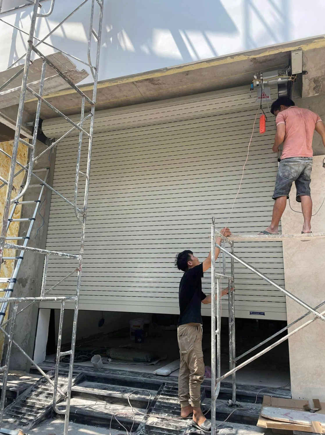 Thợ đang lắp đặt cửa cuốn tự động màu trắng cho mặt tiền nhà phố đang xây dựng