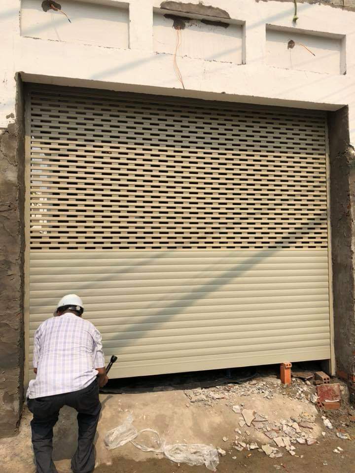 Cửa cuốn tôn màu kem đang lắp đặt cho mặt tiền nhà, thợ thi công chỉnh sửa phần chân cửa